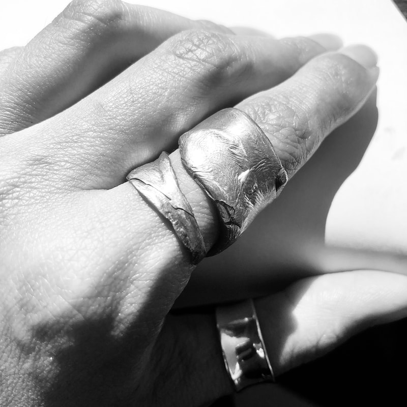 Close up black and white image of a SKINS Collection ring on an index finger showing detailed skin texture on both the hand and the ring