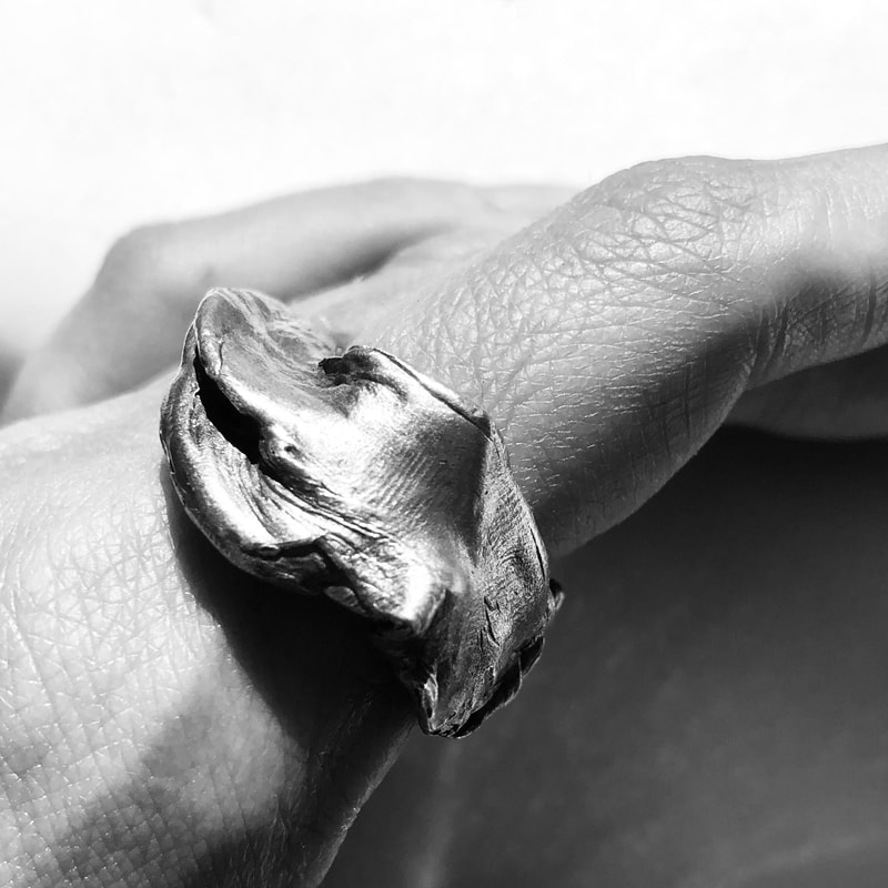Close up black and white image of a SKINS collection ring on a finger showing detailed skin texture on the finger and the ring